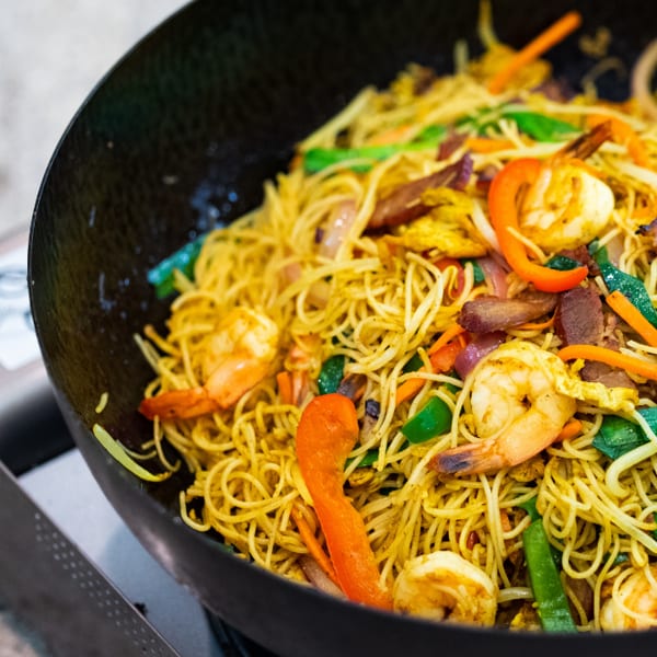 Stir-fried noodles with shrimp, colorful vegetables, and meat in a black wok.