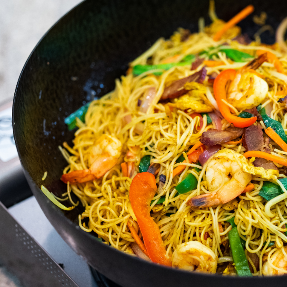 Stir-fried noodles with shrimp, colorful vegetables, and meat in a black wok.