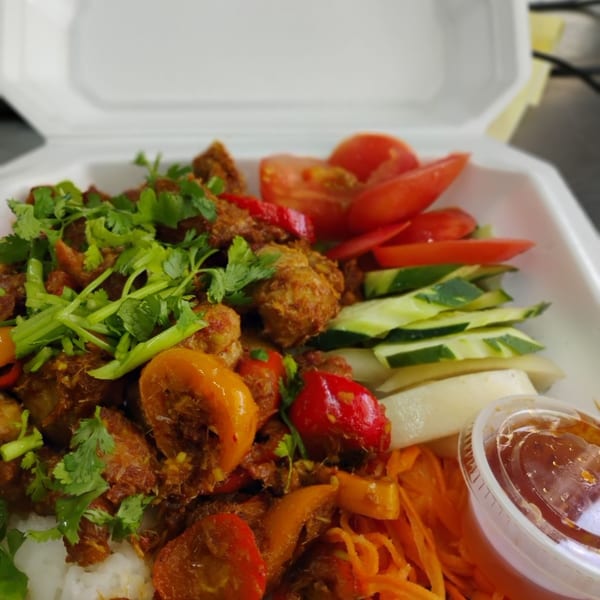 Spicy meat and pepper stir-fry with rice, fresh vegetables, and dipping sauce in a takeout container.
