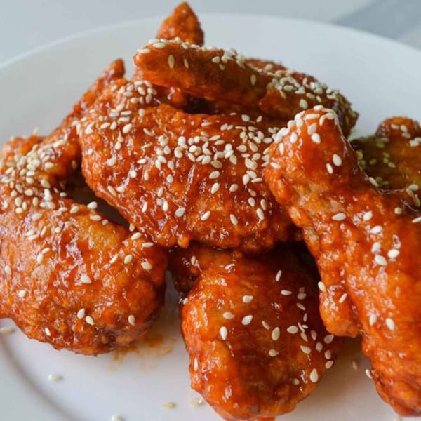 Red-glazed chicken wings generously sprinkled with white sesame seeds on a white plate.